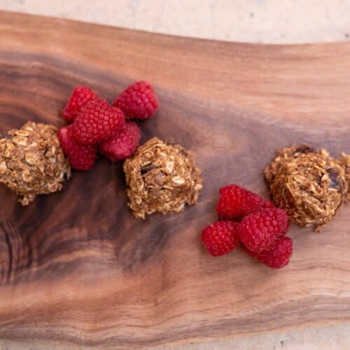 Three anti-inflammatory protein balls made with oats and peanut butter on a walnut board with fresh raspberries