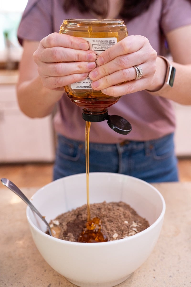 Honey being poured from a jar into a bowl of oats and peanut butter