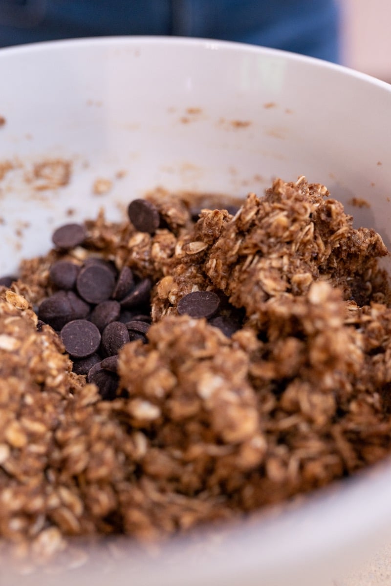 Dark chocolate chips added to the oat and peanut butter mixture in a mixing bowl