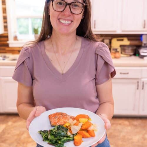 Sarah Bullard, MS,RD holding a balanced anti-inflammatory meal with salmon, vegetables, and greens in a home kitchen.