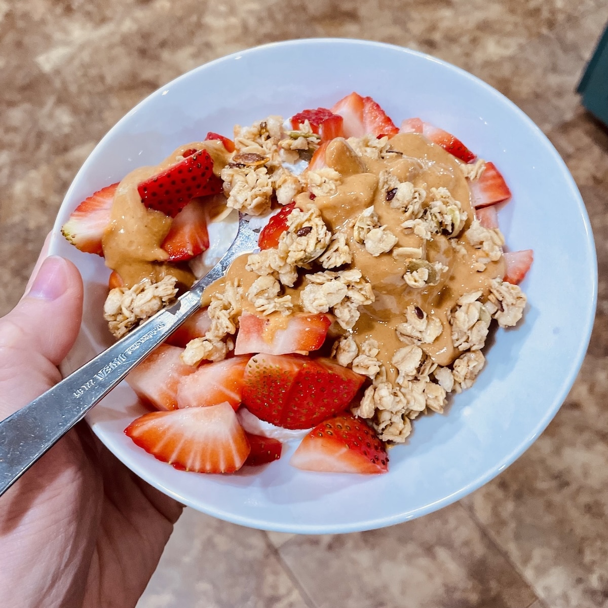 Plain Greek yogurt bowl topped with chopped strawberries, melted natural peanut butter, and whole grain granola.