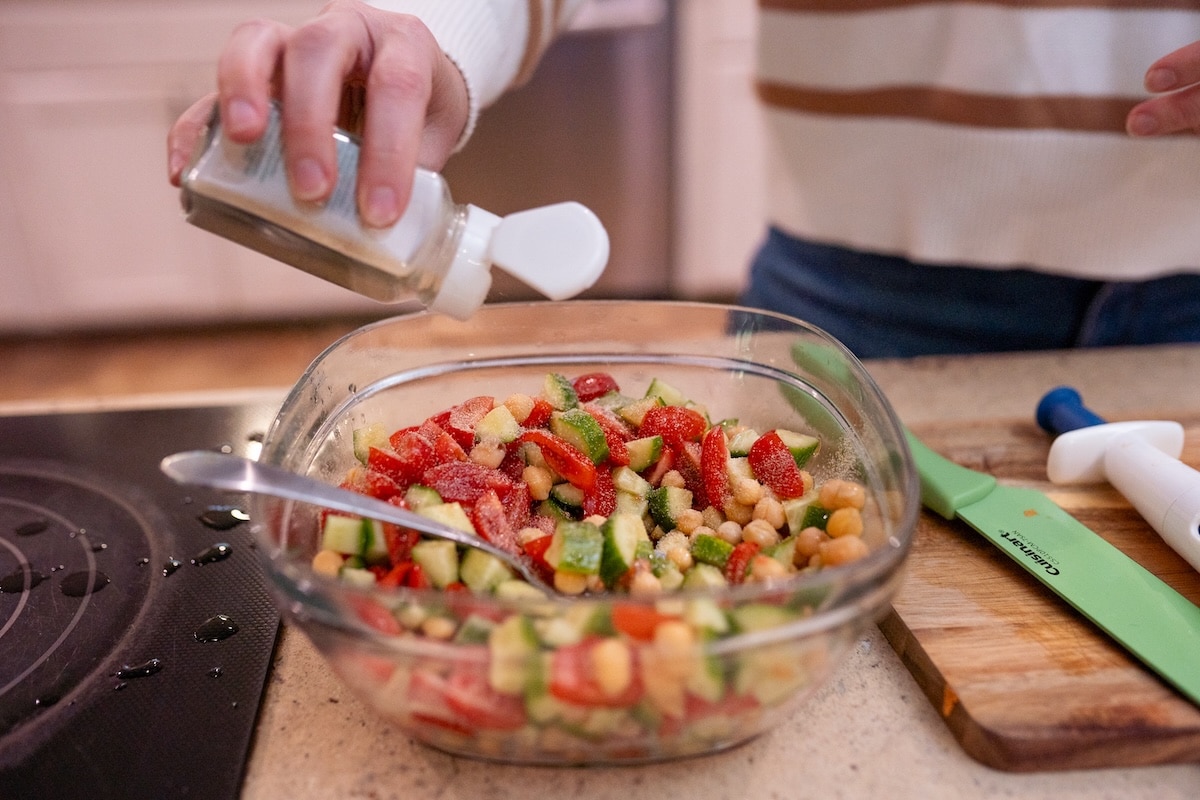 Preparing Mediterranean chickpea salad with chickpeas, cucumbers, tomatoes, peppers, olive oil, and lemon juice.