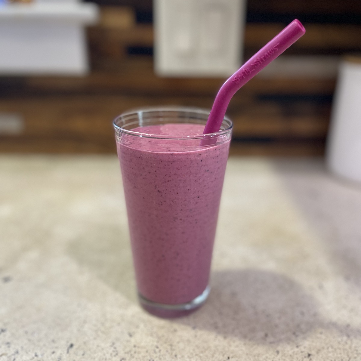A pink berry smoothie in a glass with a straw