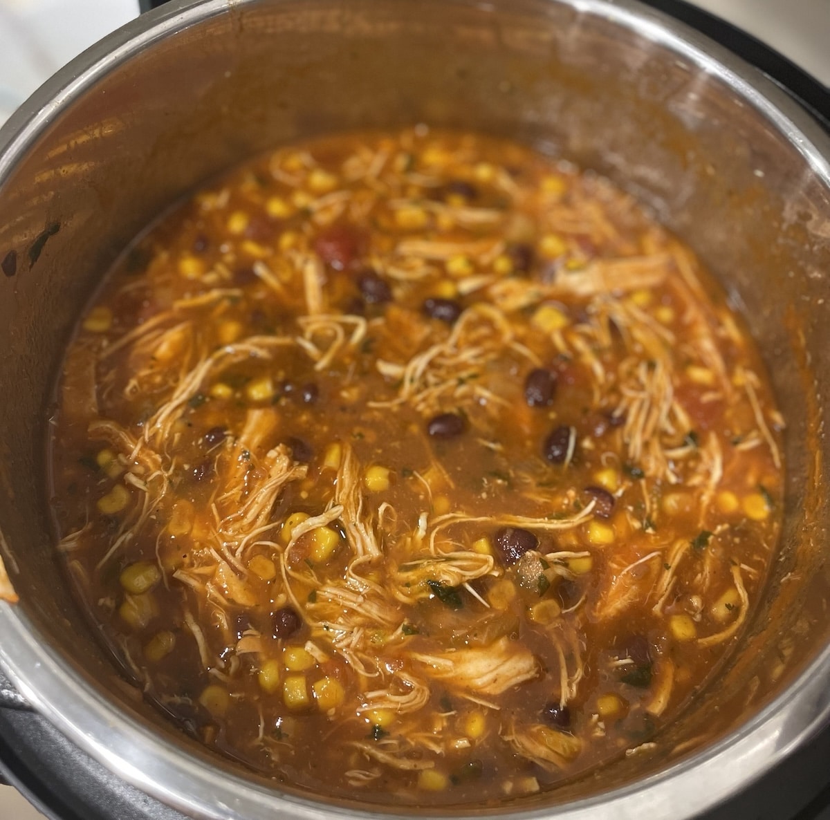 Finished chicken tortilla soup in an Instant Pot, full of shredded chicken, corn, black beans and cilantro.