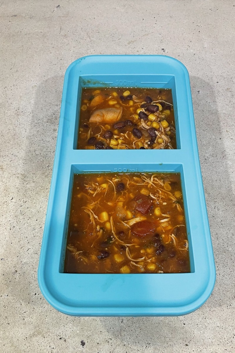 Chicken tortilla soup portioned into two 2 cup (500mL) Souper Cubes compartments, ready for the freezer, with shredded chicken, corn and black beans visible.