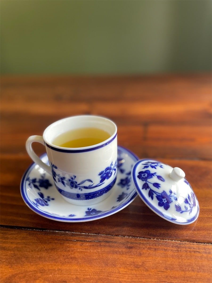 Green tea in a blue-and-white floral porcelain cup with a saucer and lid on a wood table.