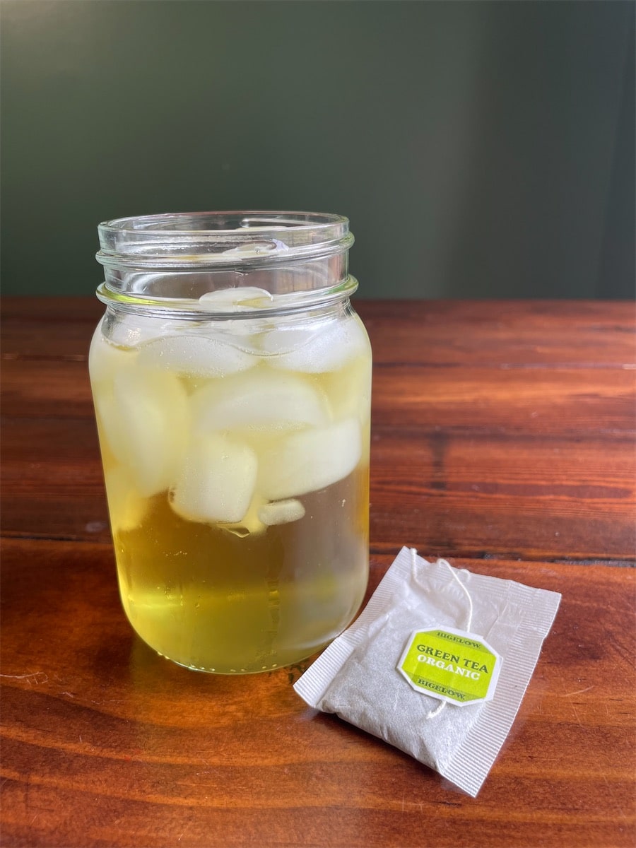 Iced green tea in a mason jar with a Bigelow organic green tea bag on a wood table.