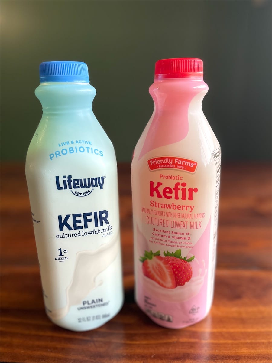 Bottles of Lifeway plain unsweetened kefir and Friendly Farms strawberry kefir on a wood table.