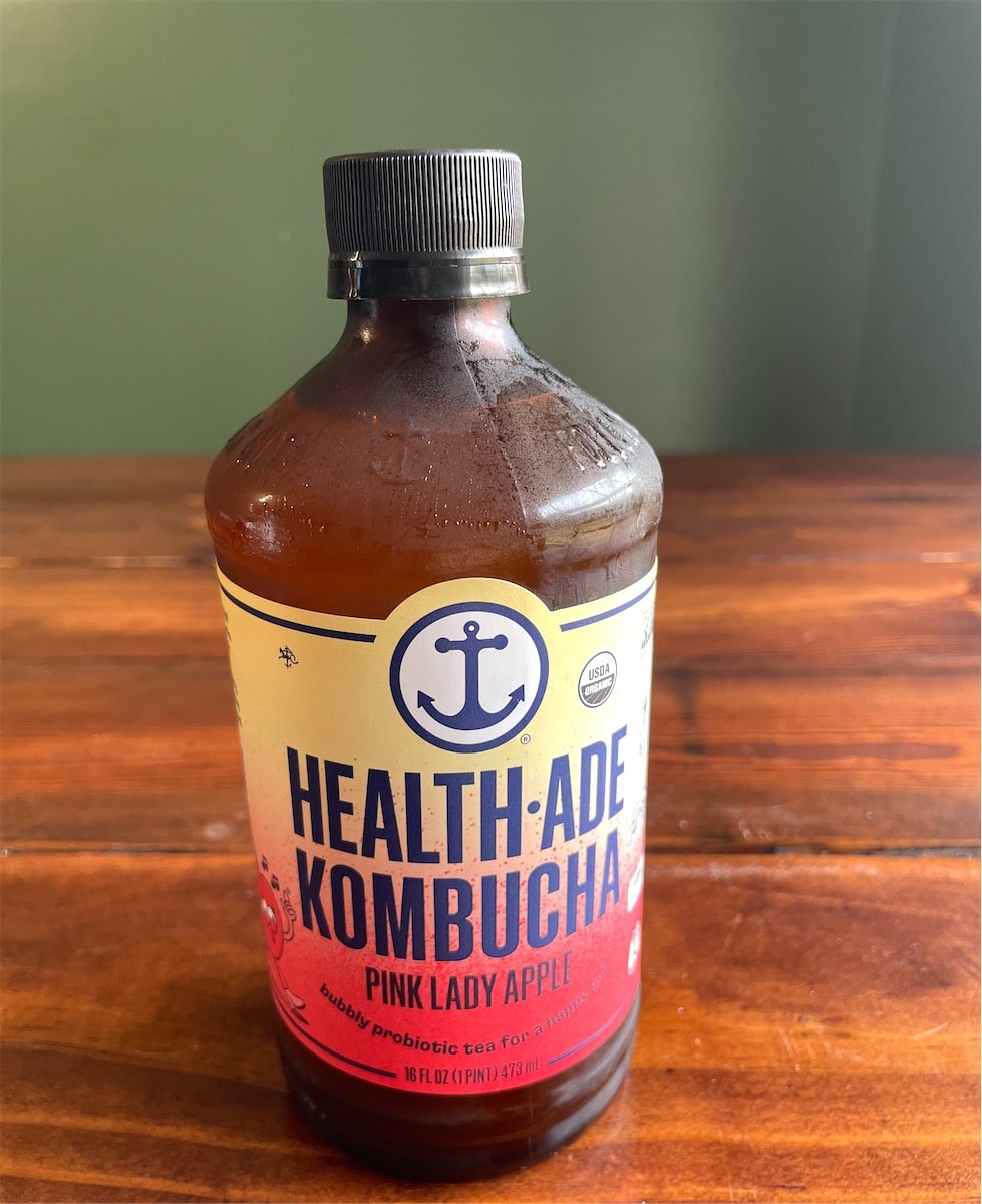 Bottle of Health-Ade Pink Lady Apple kombucha on a wood table.