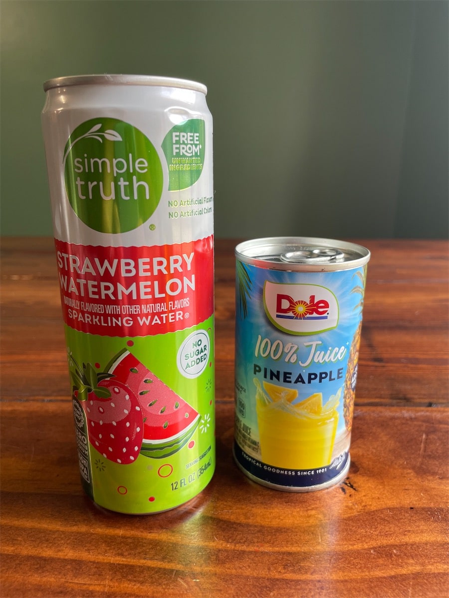 A can of Simple Truth strawberry watermelon sparkling water next to a small can of Dole 100% pineapple juice.