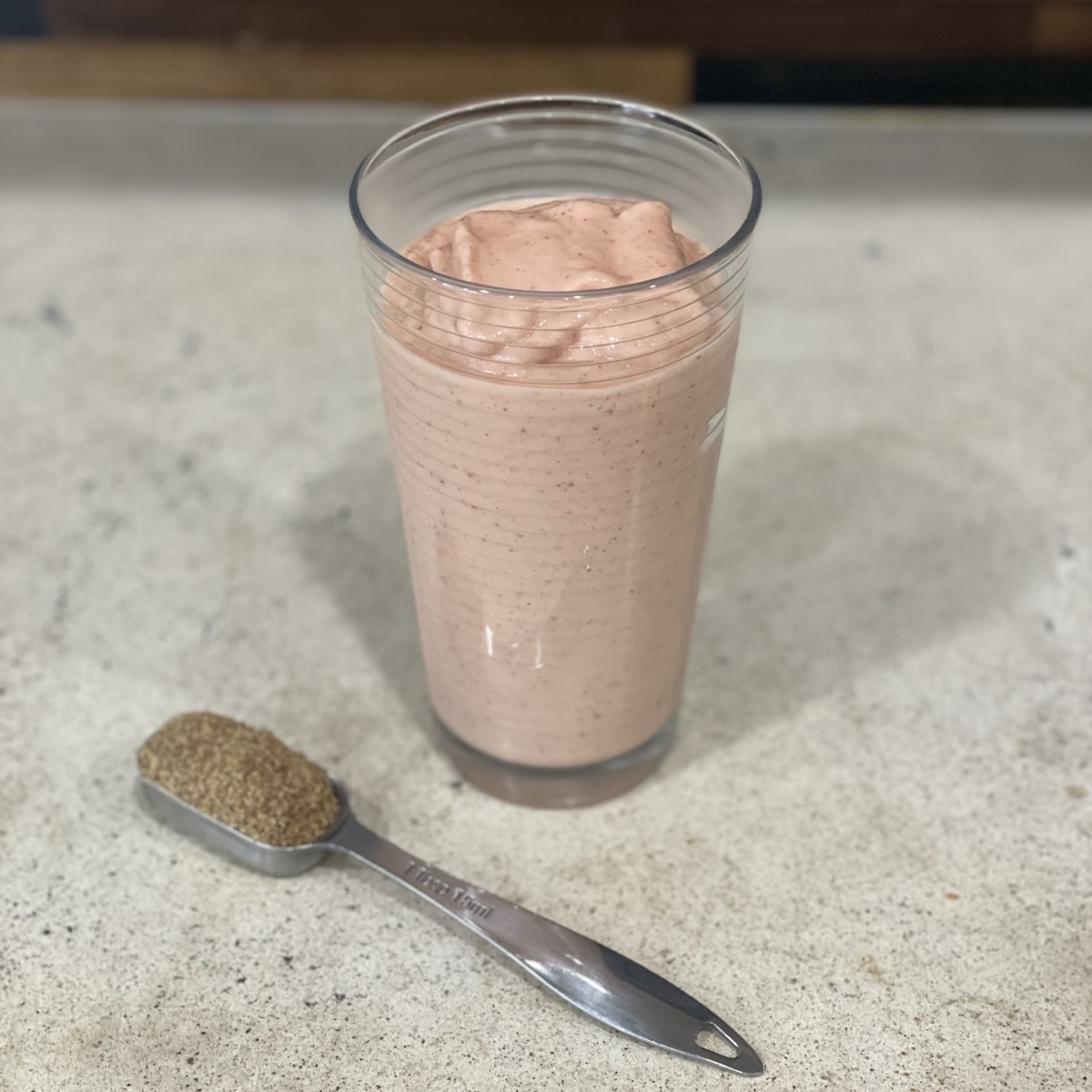 Pale peach tropical smoothie in a tall glass on a kitchen counter, with a tablespoon of ground flaxseed beside it