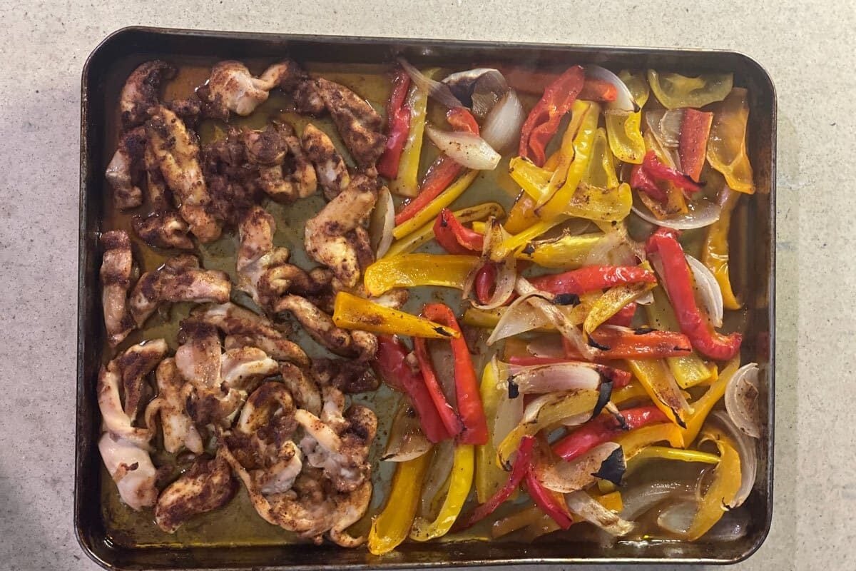 Roasted chicken fajitas on a sheet pan with charred red and yellow peppers and onions