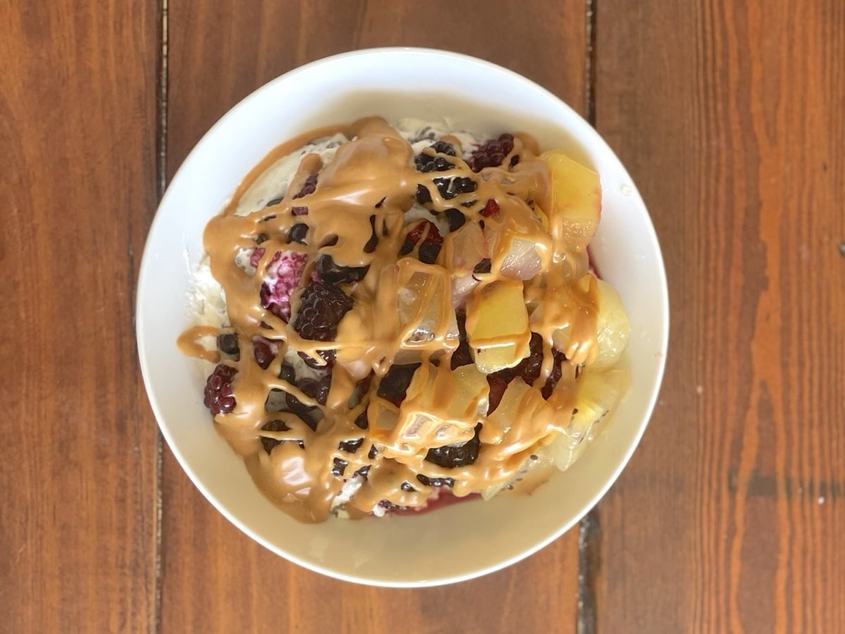 Greek yogurt bowl with mixed berries, golden kiwi and a peanut butter drizzle, viewed from above