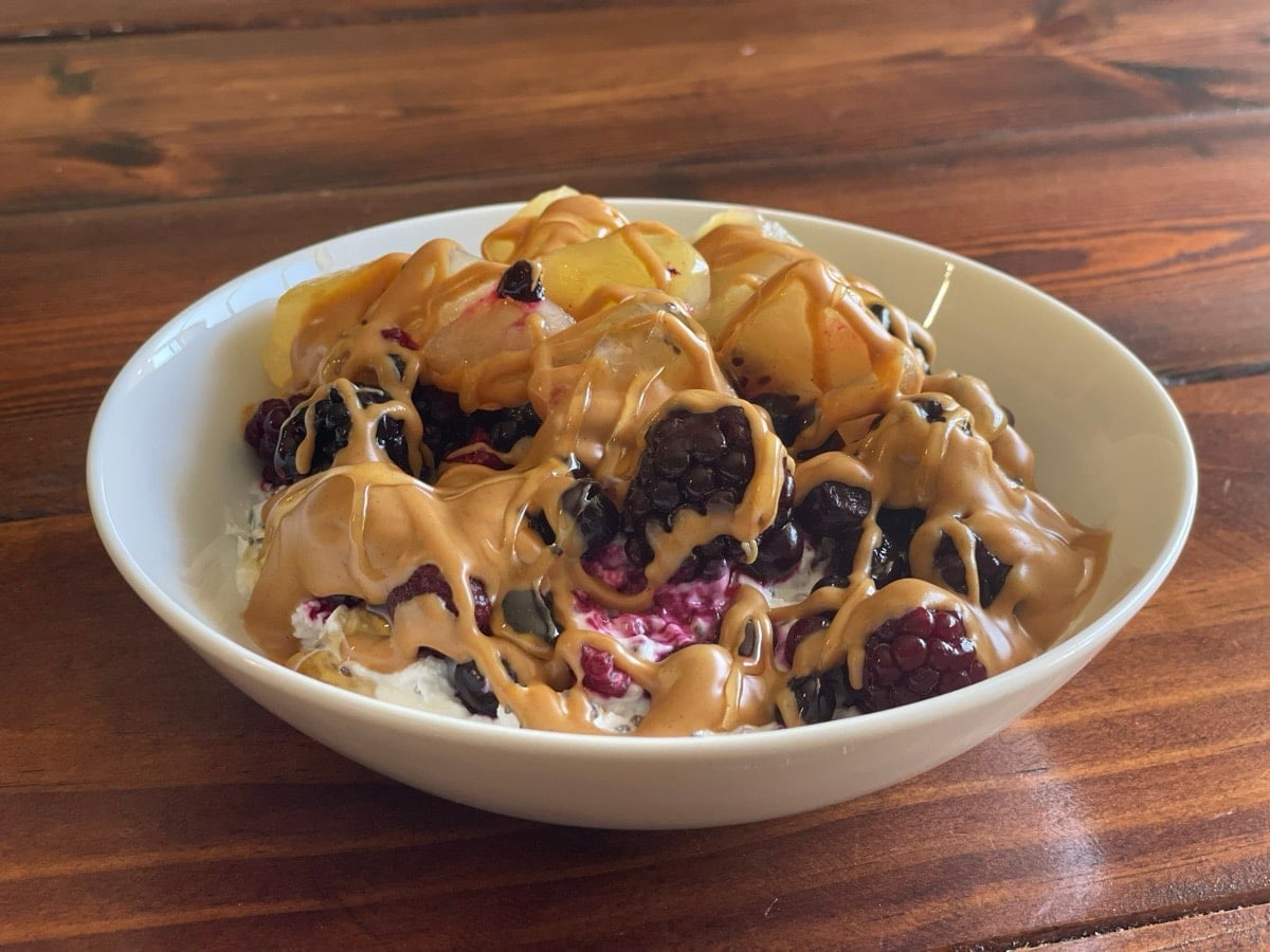 Peanut butter yogurt bowl with berries and kiwi, finished with a drizzle of honey